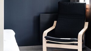 Ein Zimmer mit einer dunkelblauen Wand, einem gerahmten Bild eines Sonnenuntergangs, einem Holzstuhl und einem Fenster mit Vorhängen.