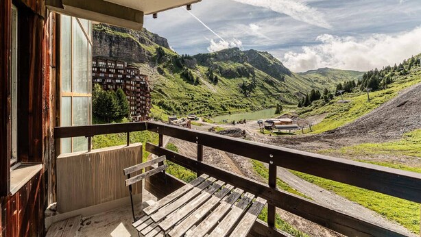 Ein Holzbalkon mit Blick auf eine Berglandschaft, einschließlich eines Sees und einem Gebäude mit vielen Fenstern.