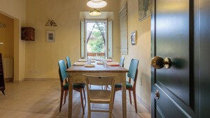 Un comedor con una mesa dispuesta para cuatro personas, sillas, una lámpara colgante y una puerta con picaporte de latón.
