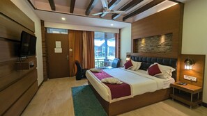 A hotel room with a large bed, a television, a wooden headboard, a small bedside table, and a view of the outdoors. - Gondwana Jungle Resort (Chimur)
