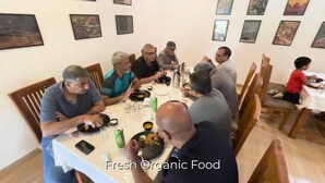 Un groupe de personnes est réuni autour d’une table, où l’on peut voir différents plats et boissons. Elles se trouvent dans une pièce dont les murs sont ornés de tableaux encadrés.