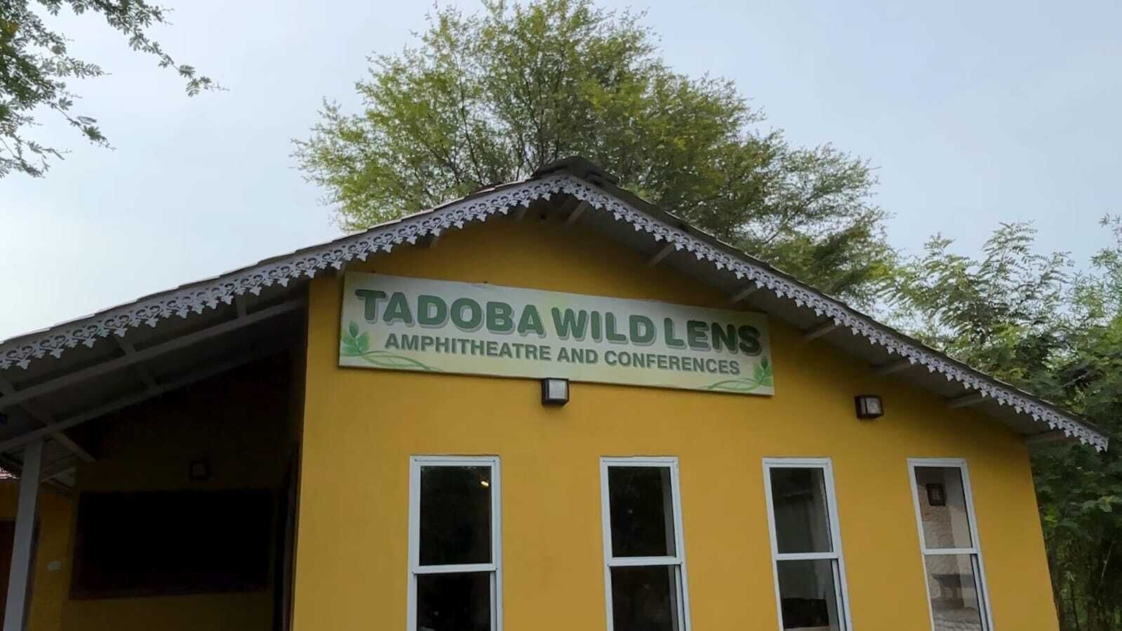 A yellow building with a sign reading "TADOBAWILD LENS Amphitheatre and Conferences".