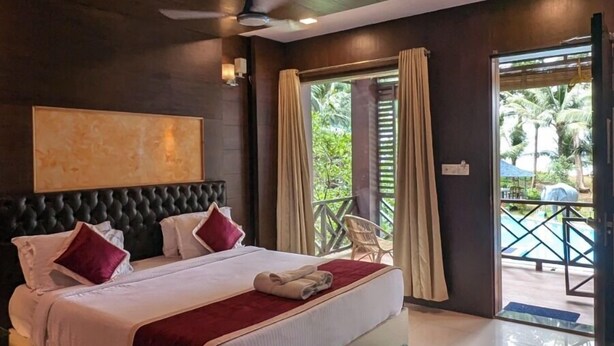 Une chambre spacieuse avec un grand lit, un ventilateur de plafond et une vue sur la piscine, visible à travers la porte-fenêtre coulissante.
