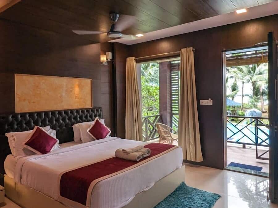 Une chambre spacieuse avec un grand lit, un ventilateur de plafond et une vue sur la piscine, visible à travers la porte-fenêtre coulissante.