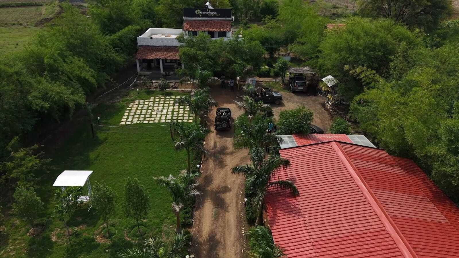Uma propriedade rural com calçada pavimentada, um edifício com telhado vermelho e uma estrutura com telhado branco.