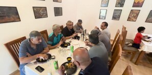A group of people dining at a table with various dishes and drinks, in a room with framed pictures on the wall. - Gondwana Jungle Resort (Chimur)