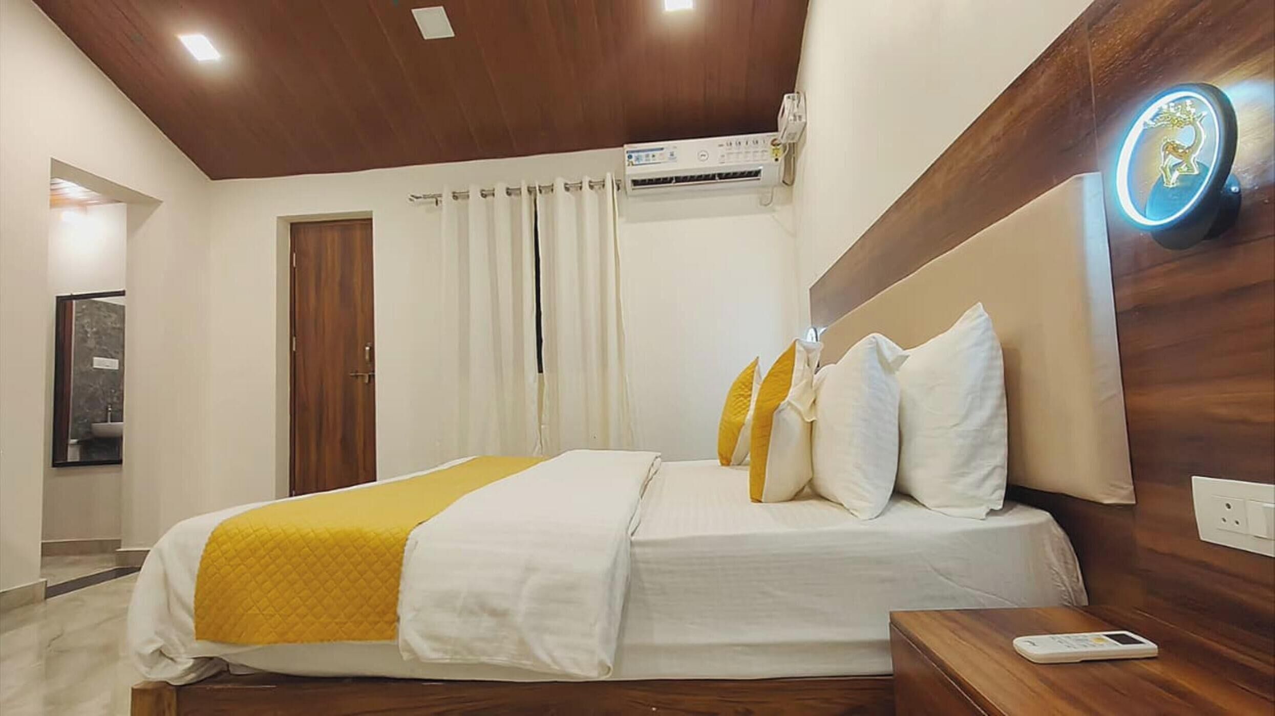 A hotel room with a bed, a bedside table, an air conditioning unit, a mirror, and a wooden headboard.