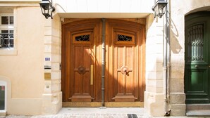 A double wooden door with a brass handle, flanked by two black lantern-style lights. - Hôtel La Particulière (Caen)
