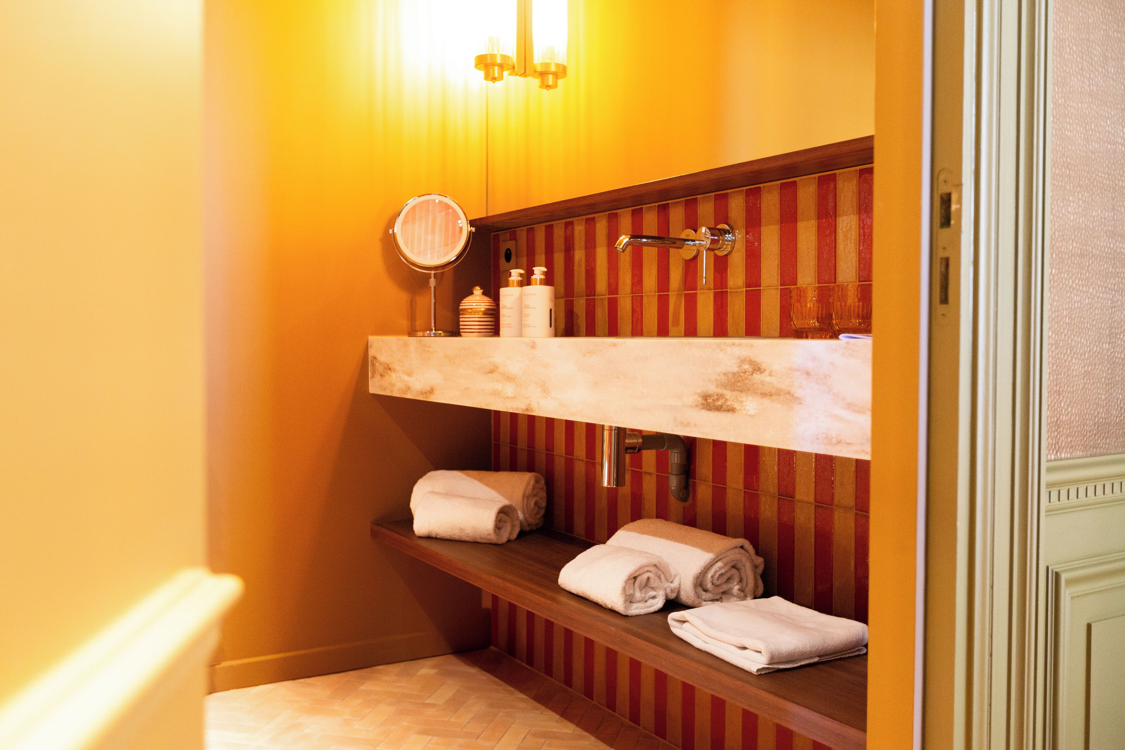 Une salle de bain avec un meuble-lavabo en bois, un miroir et des étagères où sont rangées les serviettes.
