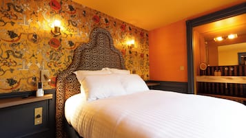 Habitación de hotel con una cama grande, un cabecero con un diseño decorativo, una pared con un mural detallado y un espejo sobre la cama.