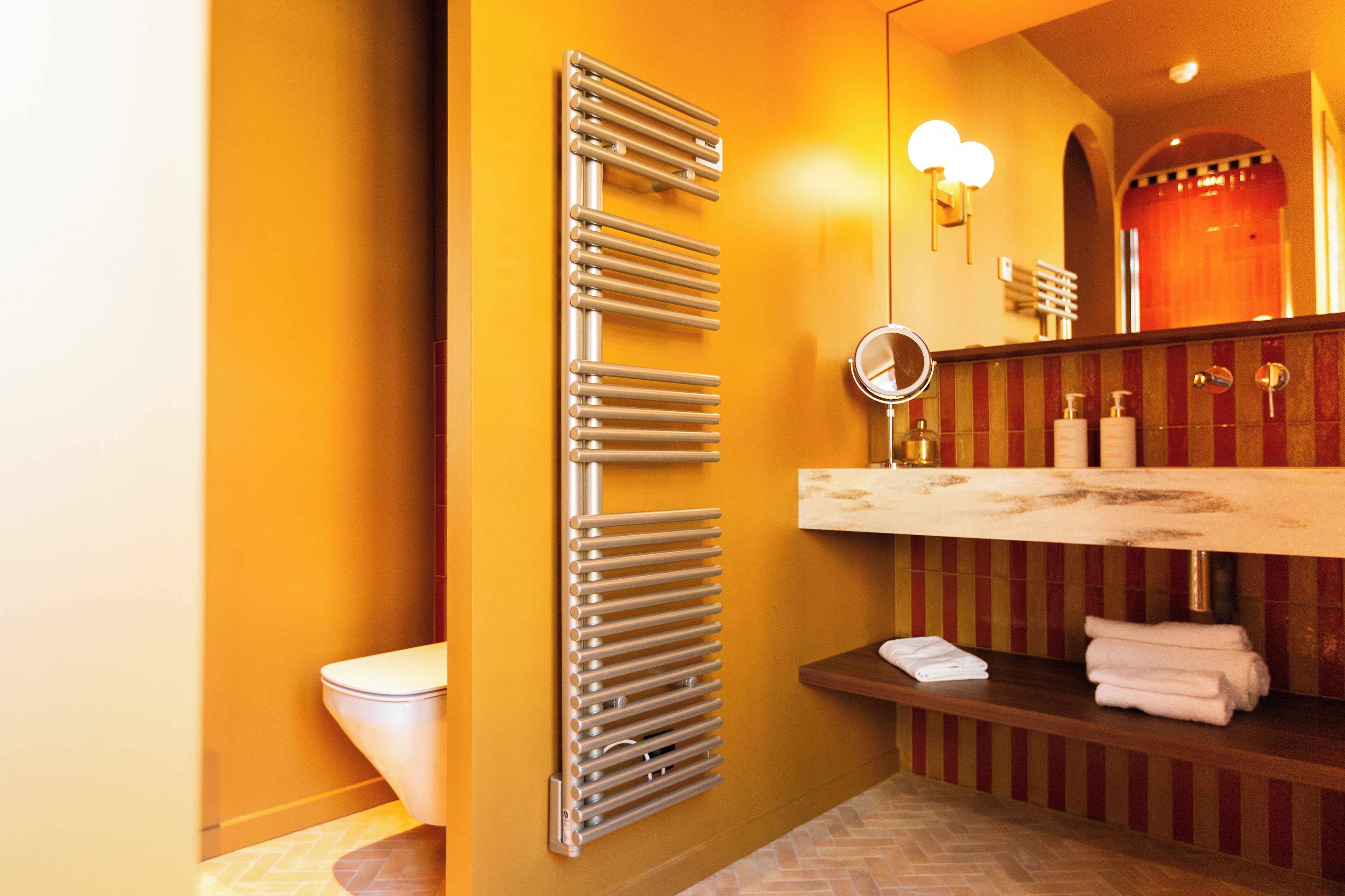 A bathroom with a modern design, featuring a toilet, a towel rack, a sink with a mirror, and a shower area.
