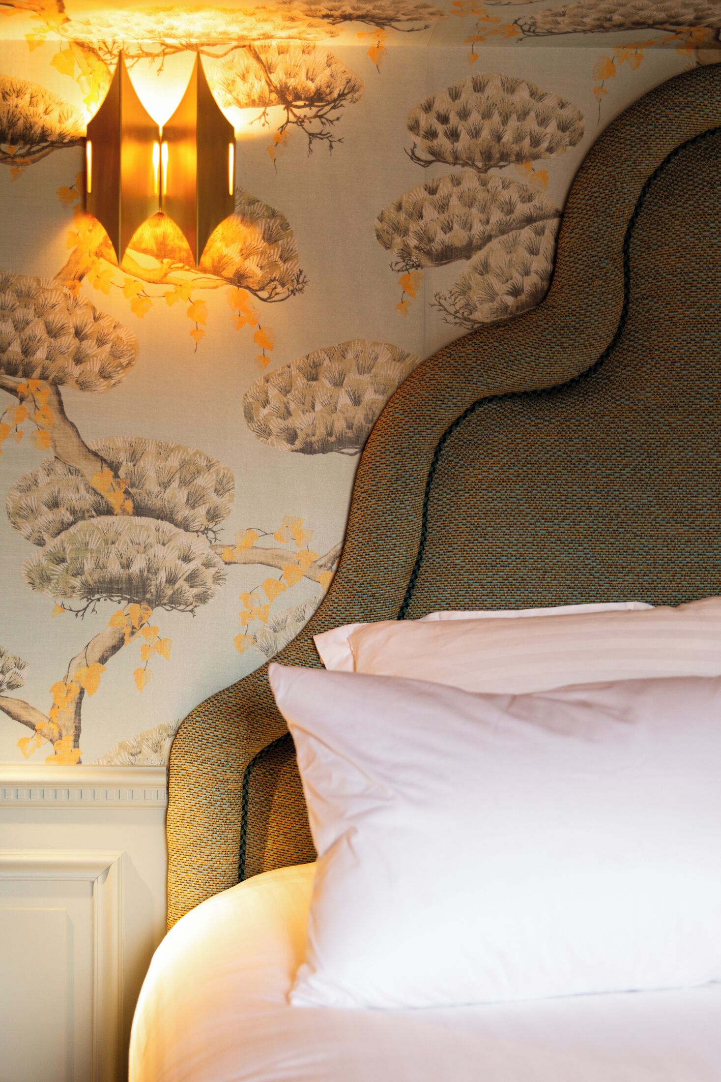 A bed with white linens, a textured headboard, and a wall with a floral wallpaper pattern.