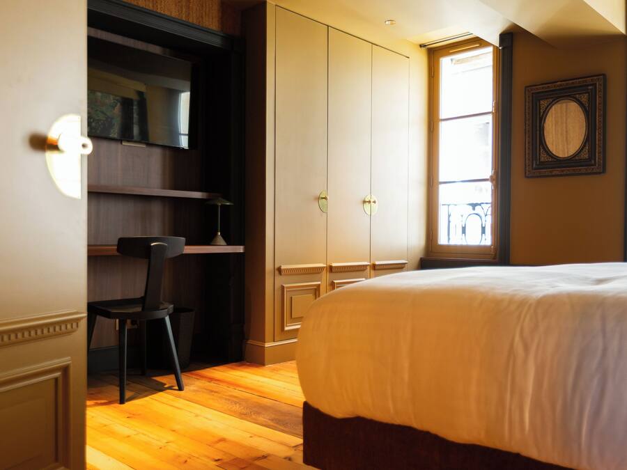 Un dormitorio con cama, una silla, armario y ventana.