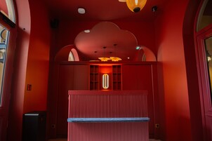 Um quarto com paredes vermelhas, uma luminária central, uma mesa pequena e um alto-falante.