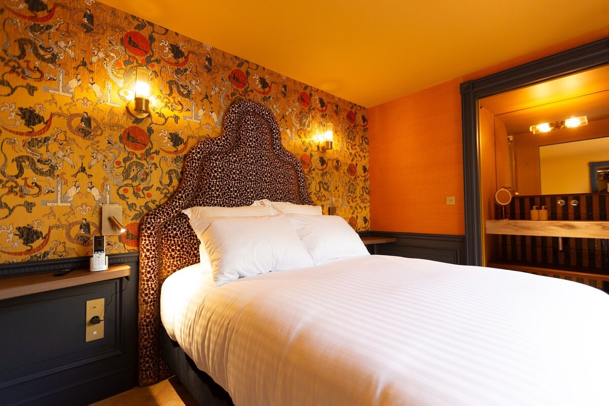 Una habitación de hotel con una cama grande, un cabecero de diseño único, una pared con un mural detallado y un espejo sobre la cama.