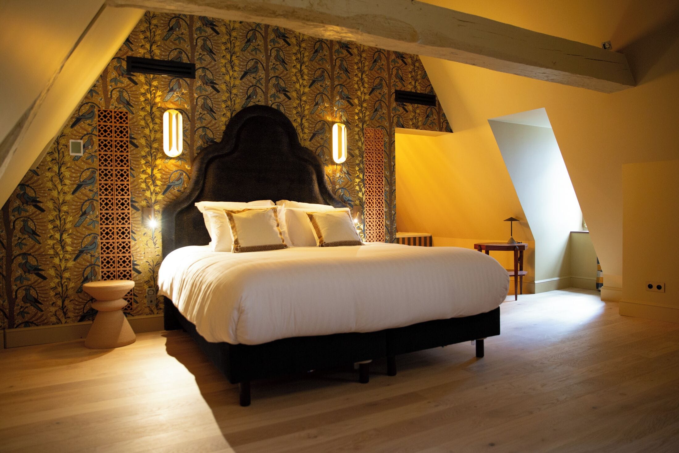 A bedroom with a large bed, a wooden floor, and a sloped ceiling with a skylight.