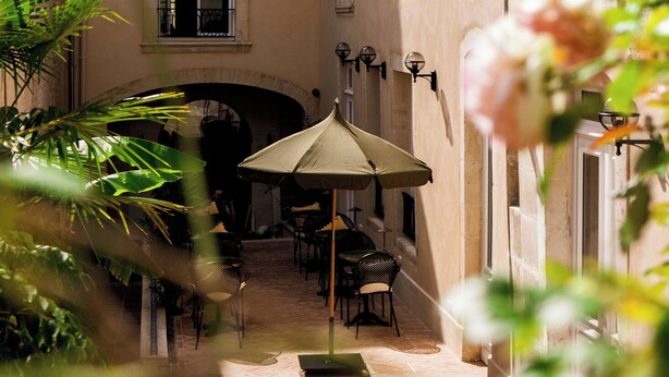 A courtyard with a table and chairs, a covered seating area, and a building with arched windows and a balcony. - Hôtel La Particulière (Caen)