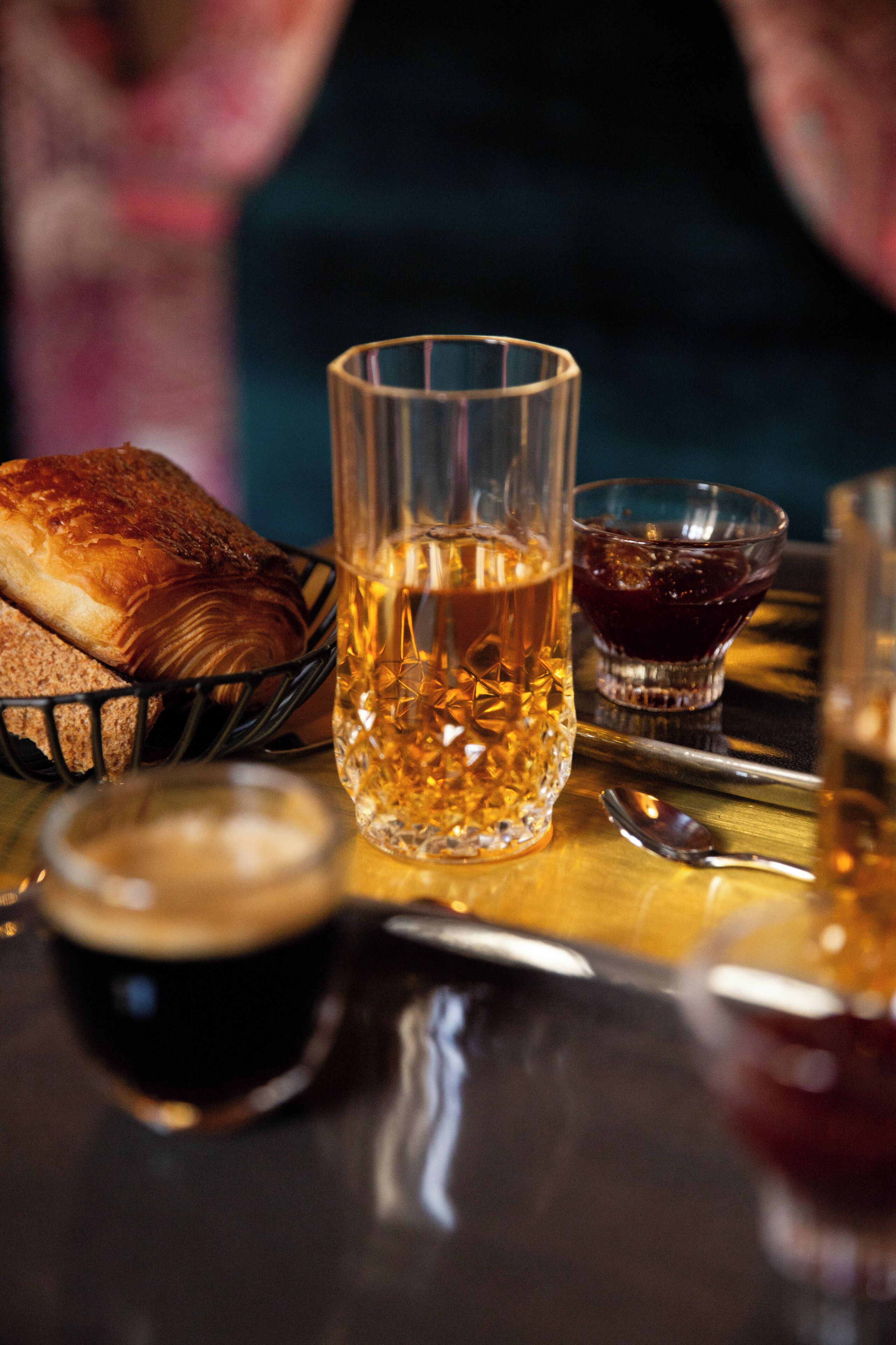 Une table avec un verre contenant un liquide ambré, un petit bol rempli d’une substance rouge foncé, une miche de pain et une tasse contenant un liquide foncé.