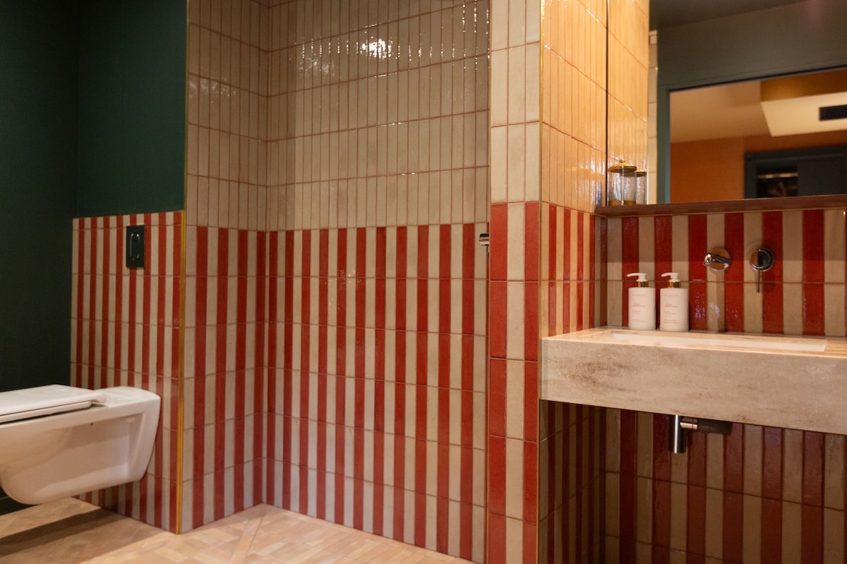 A bathroom with striped tile walls, a toilet, and a sink with toiletries.