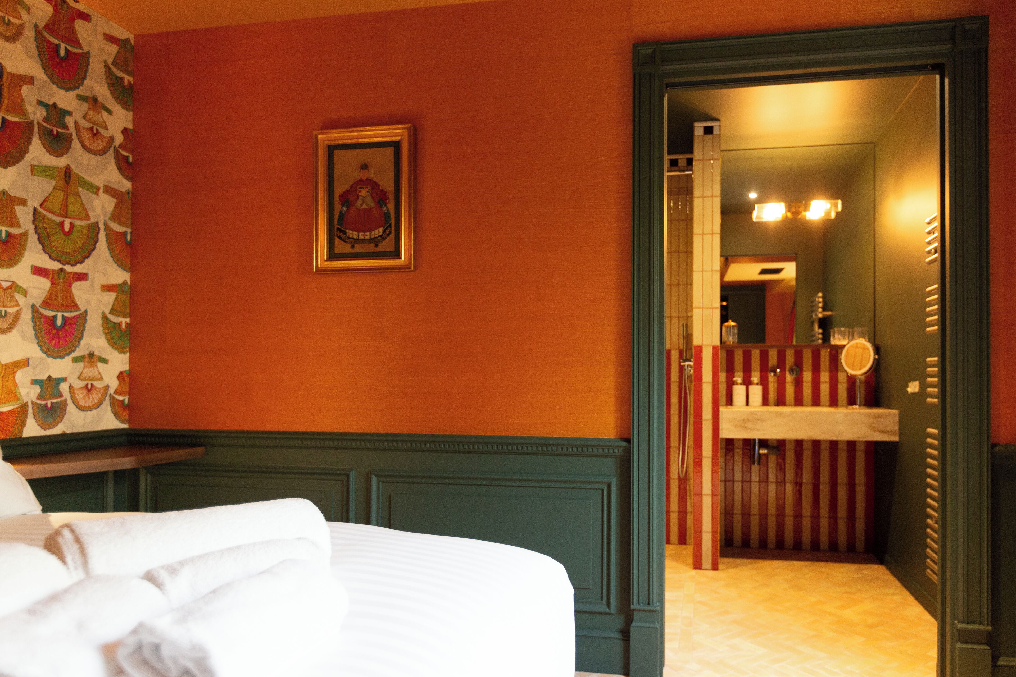 A hotel room with a bed, a framed picture on the wall, and a bathroom visible through an open door.