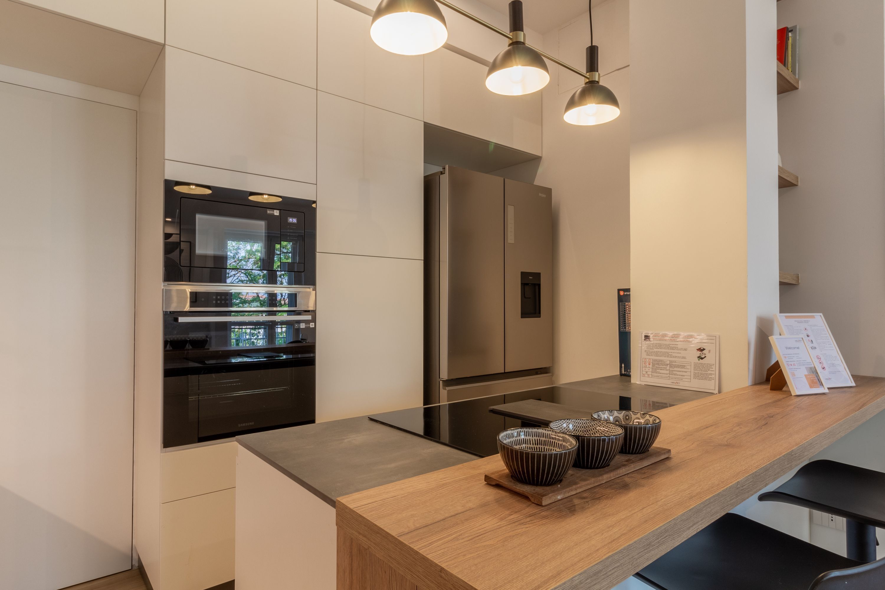 A modern kitchen with stainless steel appliances, a wooden countertop, and hanging pendant lights.