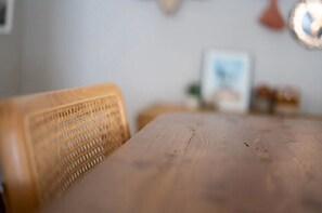 A wooden table with a woven chair in a room with a light-colored wall and a framed picture. - Chic Boho Bungalow in Land Park! (Sacramento)