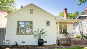 A small, single-story house with a front porch, a potted plant, and a small garden area. - Chic Boho Bungalow in Land Park! (Sacramento)