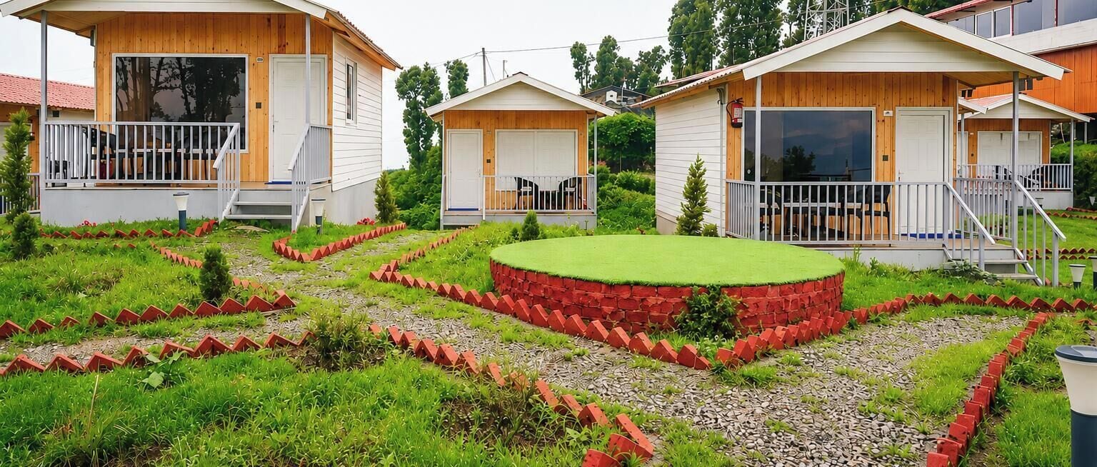 Une rangée de chalets en bois dotés de balcons, entourés d’un jardin bien entretenu avec une pelouse circulaire au centre.