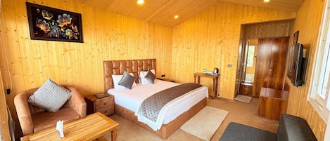 A wooden-paneled room with a bed, a sofa, a small table, and a TV.