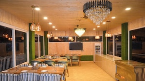 A restaurant with wooden walls, green-topped pillars, and a chandelier. Tables are set with plates and cutlery. - The Grand View Resort (Dehradun)