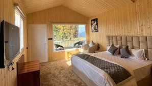 A wooden cabin bedroom with a bed, a small table, and a window. - The Grand View Resort (Dehradun)