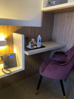 Zona de recepción de hotel con un teléfono moderno, una botella de agua, una taza y una silla morada.
