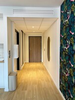 A hallway with a wooden floor, a door at the end, and a wall with a floral pattern.