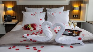 Hotelkamer met een bed, kussens, een bloemenboeket, rozenblaadjes, twee zwaanvormige handdoeken en twee champagneglazen.