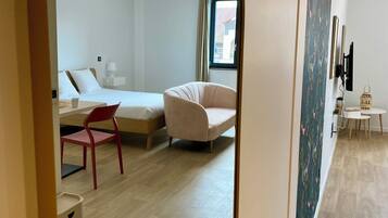 A modern hotel room with a bed, a chair, a desk, and a small table.