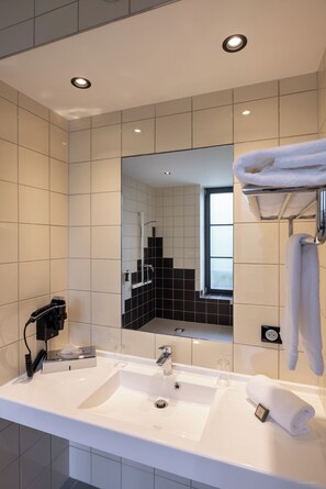 Un baño moderno con un espejo grande, dos lavamanos, un perchero para toallas y un secador de pelo.
