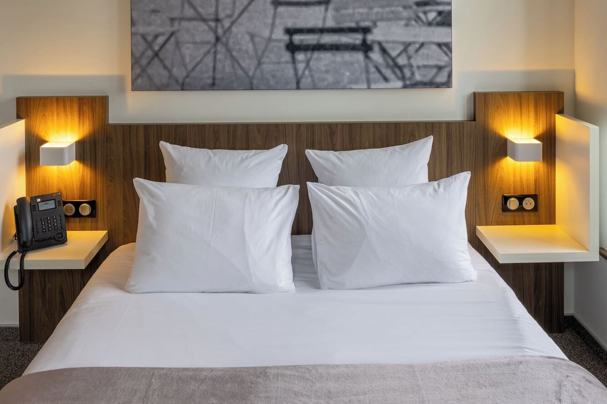 Habitación de hotel con una cama, dos mesitas de noche con lámparas, un teléfono y una obra de arte grande enmarcada en la pared.