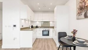 A modern kitchen with white cabinets, a built-in oven, and a dining area with a table and chairs. - CannyCity 1 Bedroom APT (London)