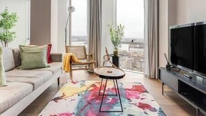 Un salon moderne comprenant un canapé, une petite table ronde, un téléviseur à écran plat et une grande fenêtre donnant sur la ville.