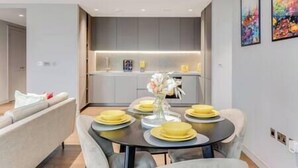 Un espace repas moderne avec une table ronde dressée pour quatre personnes, agrémentée d’assiettes jaunes et d’un vase rempli de fleurs.