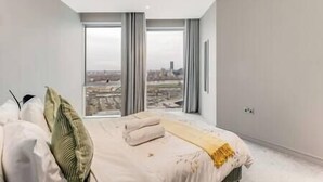 Une chambre moderne avec un grand lit, une vue sur la ville grâce à de grandes fenêtres du sol au plafond et un design minimaliste.