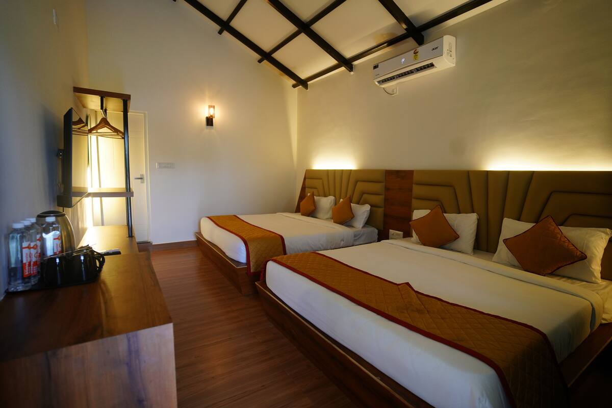 A hotel room with two beds, a wooden desk with a lamp, and an air conditioning unit on the wall.