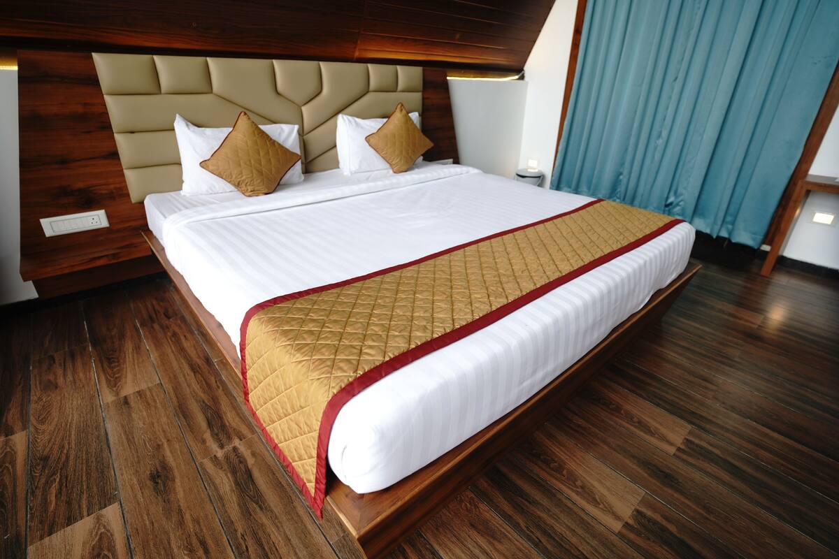 A large bed with a quilted headboard, a wooden floor, and a blue curtain.