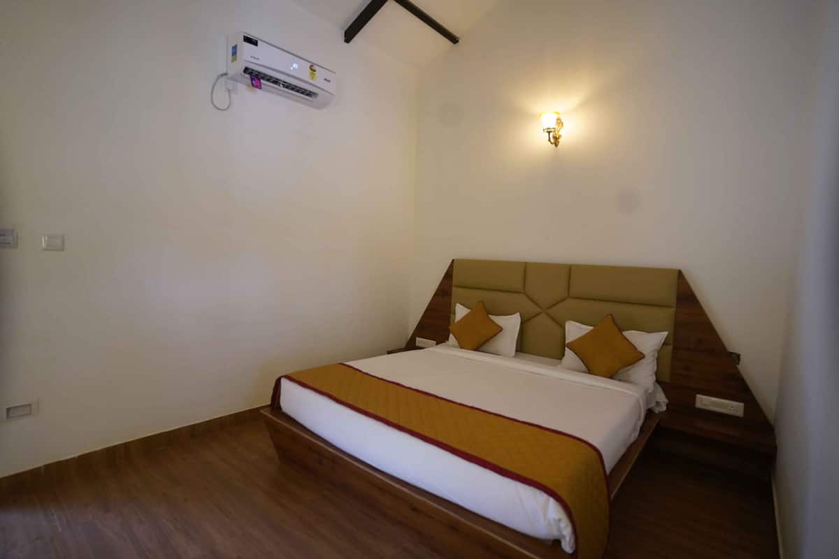 A hotel room with a bed, a wall-mounted air conditioner, and a wall sconce.