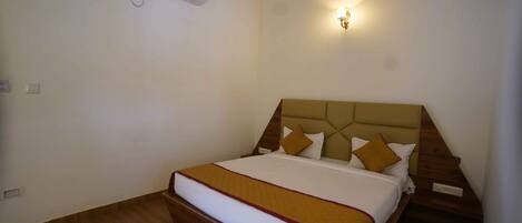 A hotel room with a bed, a wall-mounted air conditioner, and a wall sconce.