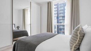 Ett modernt hotellrum med en stor säng, en spegel och utsikt över en hög byggnad.