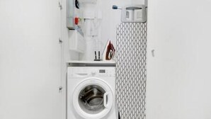 Ett kompakt och modernt tvättrum med en tvättmaskin med frontmatning, en torkställning och en liten strykbräda.