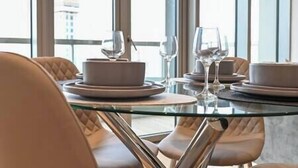 Une table à manger avec un plateau en verre, entourée de chaises en cuir, dans une pièce bien éclairée grâce à de grandes fenêtres.