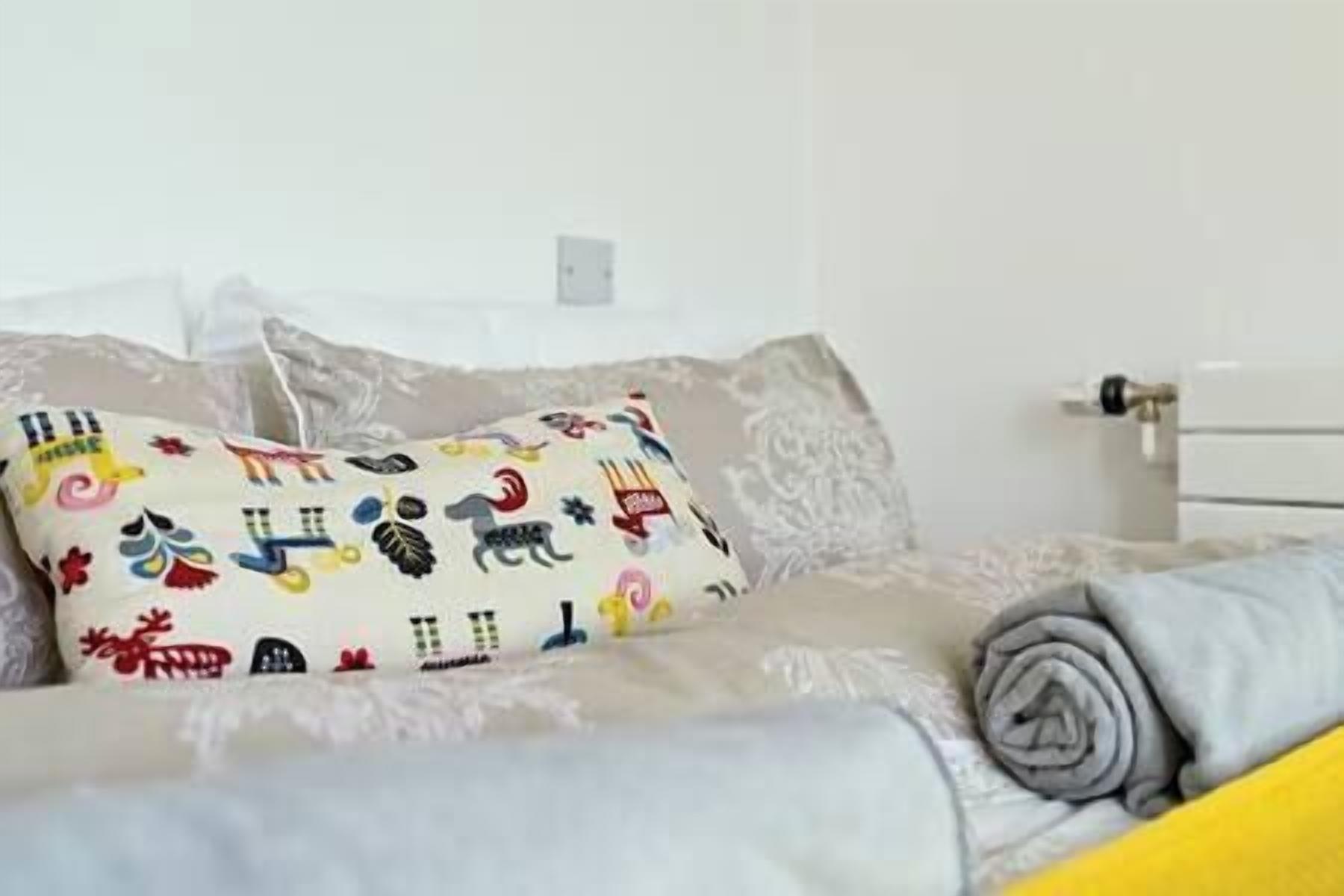 A bed with a patterned pillow, a grey blanket, and a yellow pillow.