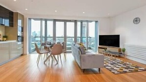 Un appartement moderne doté d’un coin repas, d’un canapé, d’une télévision et d’une grande fenêtre offrant une vue sur la ville.